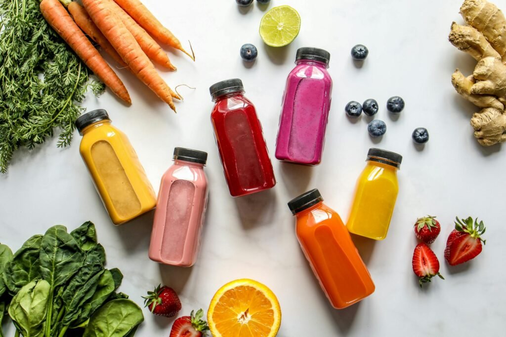 Colorful Bottles with Smoothies Beside Carrots, Ginger, Leaves and Berries